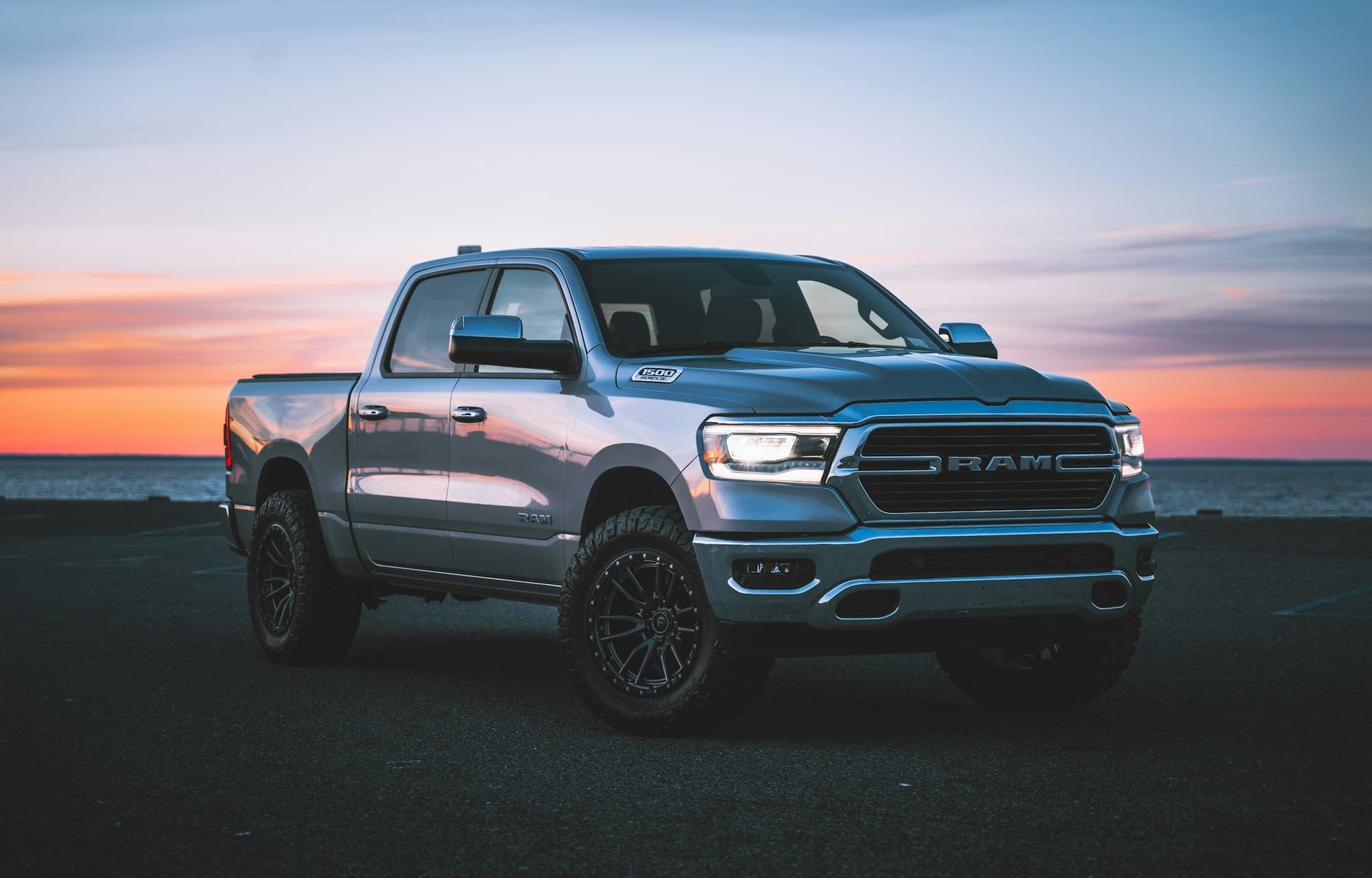 Silver Ram pickup truck parked by the ocean at sunset